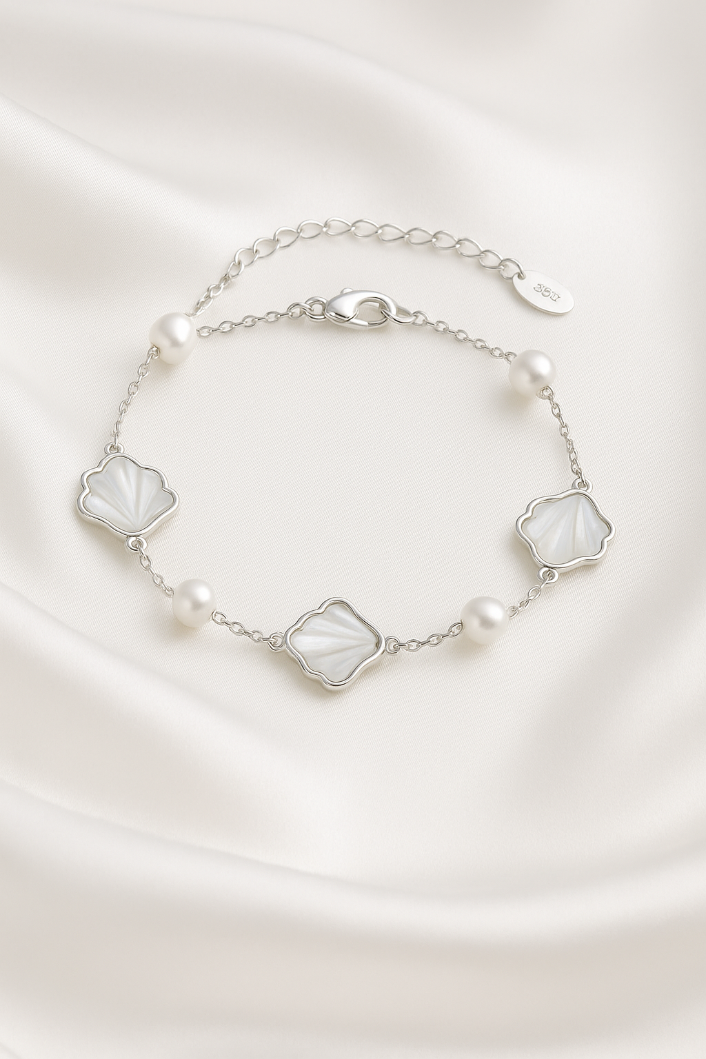 Minimalist silver bracelet featuring shell-shaped charms and freshwater pearls on silk background – elegant light luxury accessory for women.